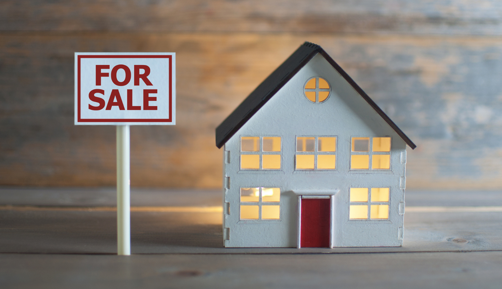 A model home on a wooden table next to a for sale sign